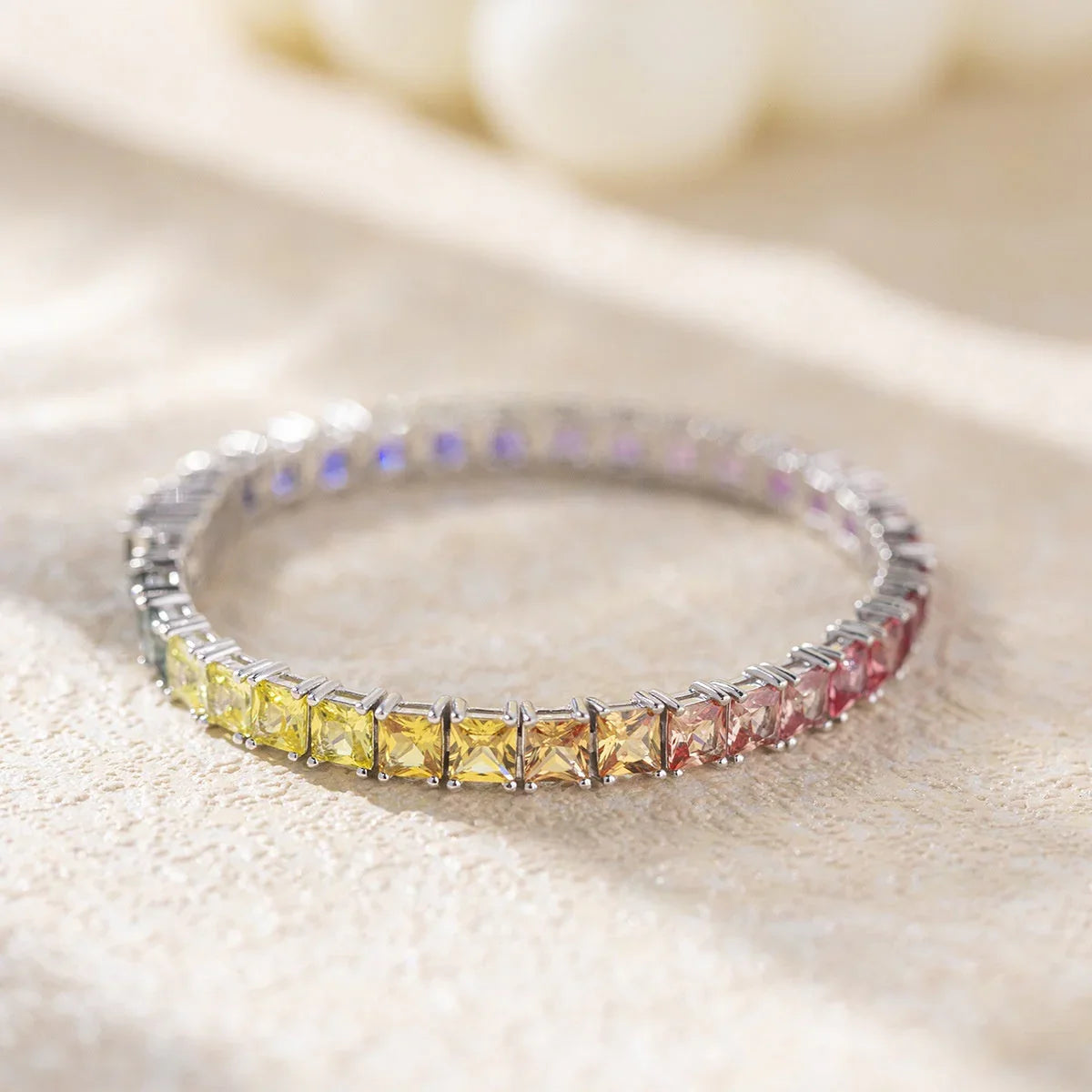 Rainbow gemstone tennis bracelet with silver setting on beige textured surface, Moment Jewels